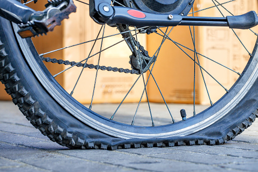 A punctured bicycle tire in selective focus against a background yellow sunlit wall in blur.