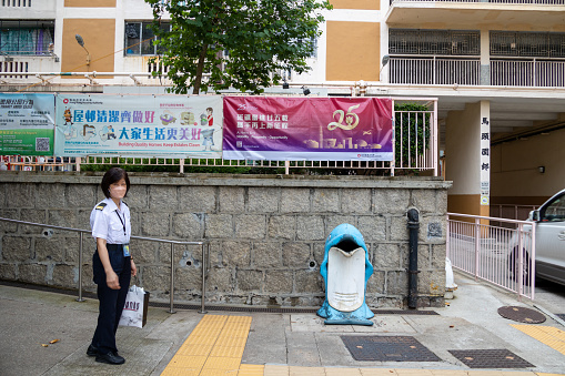 Hong Kong - June 20, 2022 : A security guard stands next to a banner with a slogan celebrating the 25th anniversary of Hong Kong's handover from Britain to China, in Ma Tau Wai Estate, Kowloon, Hong Kong.