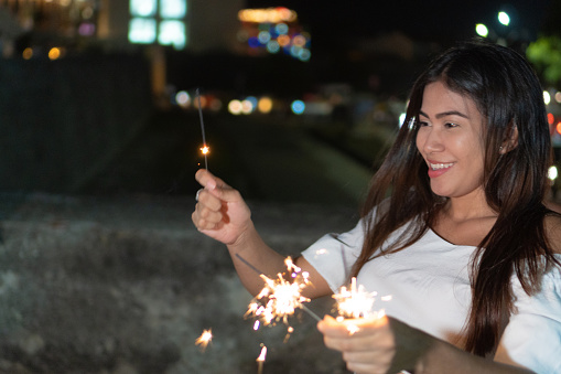 Latin woman laughing and burning flares during a nighttime party