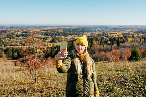 Young woman takes selfie on autumn landscape. Mountain travel.