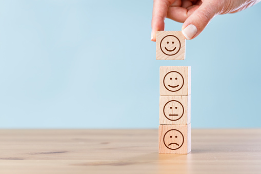 Woman hand chooses smiley face on wooden block cube