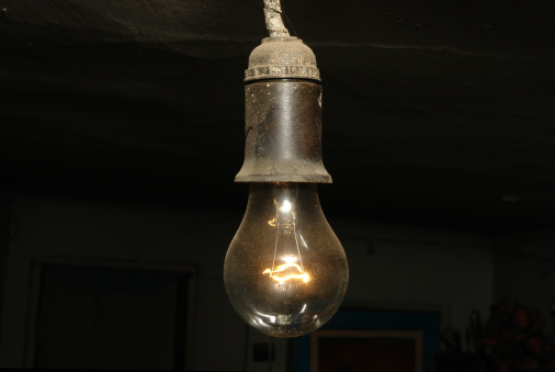 Glass sphere ceiling lighting bulb which is glowing in orange warm lighting shade. Interior object for room decoration. Close-up and selective focus.