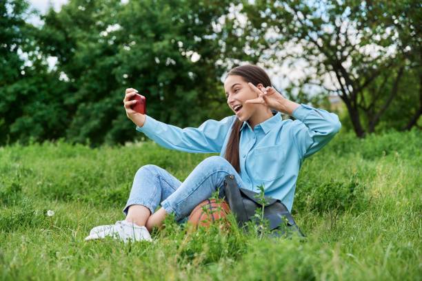 Teenage female student sitting on the grass using smartphone. stock photo