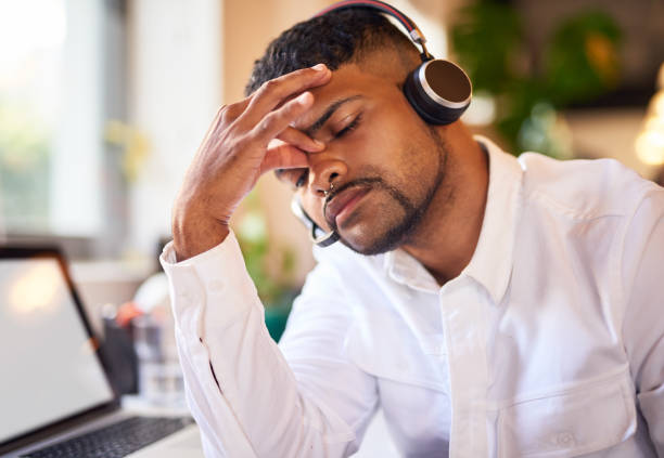 istock Male consultant looking stressed while working in a call centre. Professional businessman sitting at his desk with a serious, thinking expression sitting in front of a laptop in a modern office 1404006252
