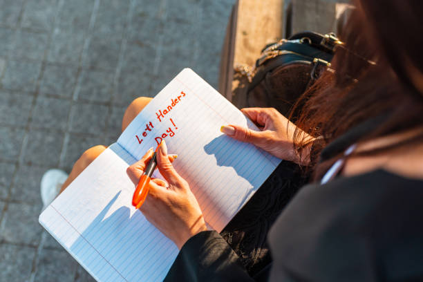 left-handers day.woman écrit dans un cahier, tient un feutre dans sa main gauche. parc extérieur du soir d’été. 13 août. closeup. - gaucher photos et images de collection