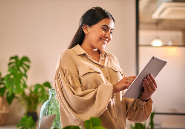 istock Indian businesswoman looking at a tablet computer while standing in the office. One young female mixed race developer holding  a tablet. Innovative entrepreneur design firm. 1404007106