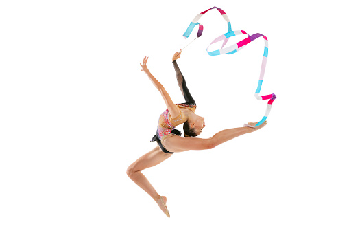 Flying with multicolored ribbon. Portrait of young sportive girl, rhythmic gymnastics artist isolated on white studio background. Concept of sport, action, aspiration, education, active lifestyle