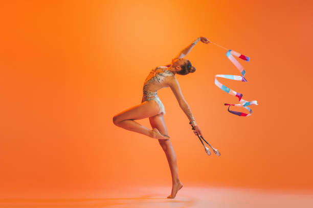 Young sportive girl, rhythmic gymnastics artist dancing isolated on orange color background. Concept of sport, action, aspiration, education, active lifestyle Dance, emotions. Young sportive girl, rhythmic gymnastics artist dancing isolated on orange color background. Concept of sport, action, aspiration, education, active lifestyle rhythm photos stock pictures, royalty-free photos & images