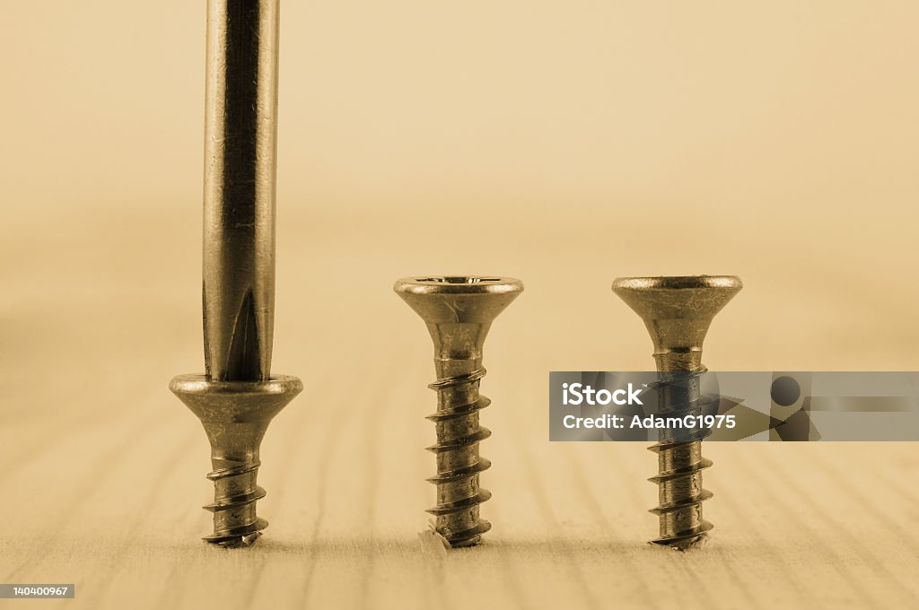 Three screws in plank of wood with screwdriver Three screws in a row and screwdriver screwing in board left one. Sepia tone Bolt - Fastener Stock Photo