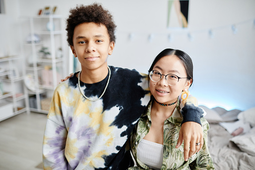 Waist up portrait of two gen Z teenagers, boy and girl smiling at camera posing together in home interior