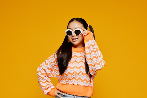Minimal waist up portrait of teenage Asian girl wearing white sunglasses over vibrant yellow background, copy space