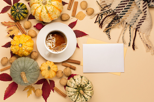 Concept of fall harvest or Thanksgiving day. Autumn composition with cup of coffee, empty white \npaper, pumpkins, nuts and cinnamons on beige background. Top view, copy space.