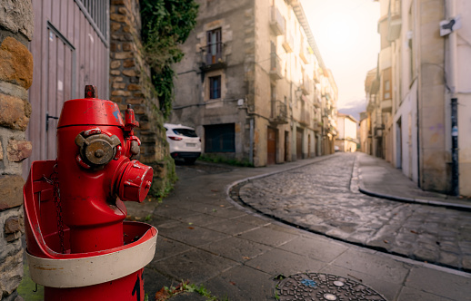 Red fire hydrant on sidewalk in Onati city, Spain. Fire hydrant on blur old building, white car, and street. Cityscape. Water supply for fire extinguisher. Fire control system of the city for safety.