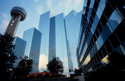 Glass wall of modern building with reflection of trees and sky clouds