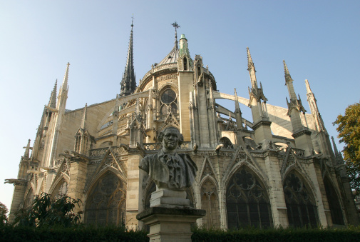 A low-angle shot of Notre Dame Cathedral from behind. Sculpted bust sits in foreground.