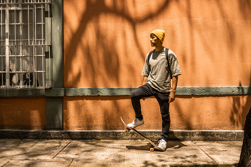 Low angle view portrait of a young Latin man wearing yellow hat looking away. He is standing his skateboard.