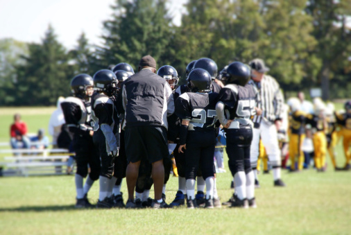 Football players in a huddle on the field with their coach.