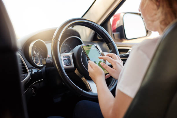 istock Female sitting inside a car texting on a phone while driving.  Reading her messages while holding her mobile device in her hand. Dangerous and risky behavior 1404022784