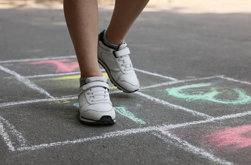 Little child playing hopscotch drawn with chalk on asphalt outdoors, closeup