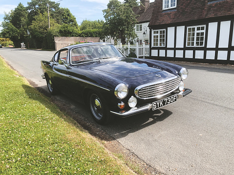 Buckinghamshire, UK - June 19, 2022: A classic dark blue Volvo 1800S from 1967 sitting at the side of the road in the village of Coleshill, Buckinghamshire. Made famous when a white version was used by Roger Moore in the iconic sixties tv show The Saint, this svelt Swedish sports coupe is still a head-turner to this day.
