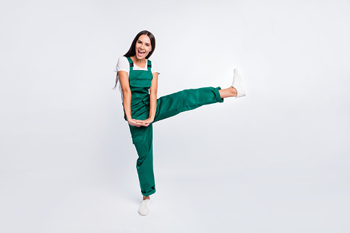 Photo of crazy party lady hold hands open mouth raise leg wear green overall sneakers isolated white color background.