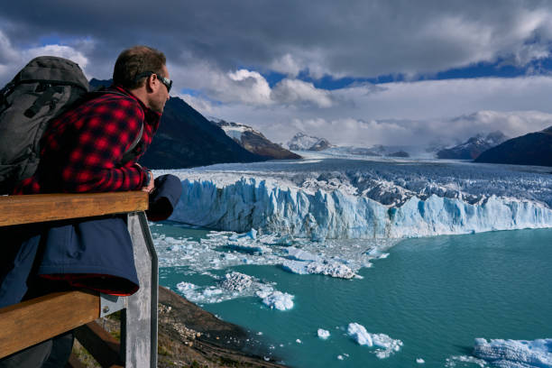young man contemplating the perito moreno glacier in patagonia argentina The Perito Moreno glacier is part of the Patagonian ice field, a field that accumulates one of the most important reserves of drinking water on earth. It is located 80 km from the city of El Calafate in the Province of Santa Cruz in Patagonia Argentina within the "Los Glaciares" National Park. The Glacier owes its fame to its continuous movement, which produces a cyclical phenomenon of advance and retreat with wonderful landslides. You will only have to sit in one of the viewpoints on the catwalks to contemplate such impressive beauty, with a panoramic view and just wait for it to happen (the landslide). patagonia argentina stock pictures, royalty-free photos & images