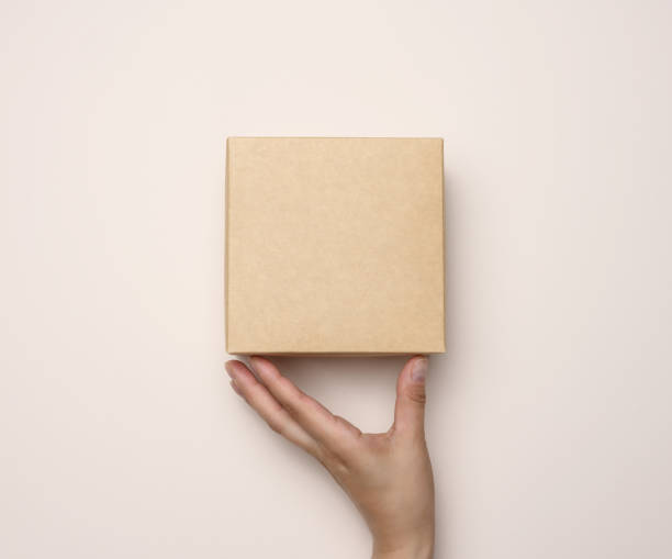 istock Female hand holding a square cardboard box on a beige background 1404025037