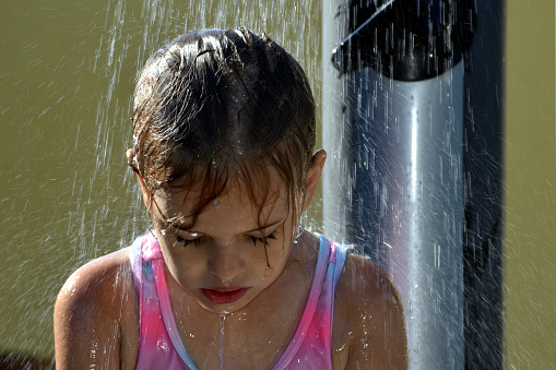 Young girl cooling down under an outside shower during hot weather in summertime