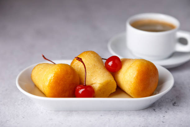 babas au rhum napolitain sur une assiette blanche avec des cerises cocktail et une tasse de café. petits muffins à la levure trempés dans du sirop avec du rhum  - little cakes photos et images de collection