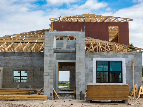 Single-family house under construction, with roof and windows in progress, and insulation panels stacked by front doorway with framed view of vicinity, in a suburban development in southwest Florida