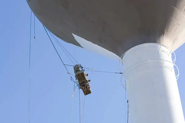 Photo of workers painting a water tank.  Dangerous job.