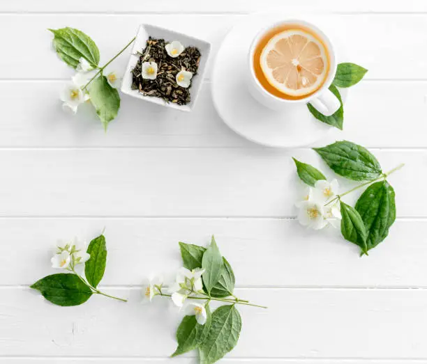 Teatime with jasmine green steaming tea, piece of lemon, jasmine flowers, space for text, topview