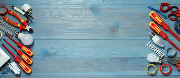 Frame of electrician's tools and accessories on light blue wooden table, flat lay. Space for text