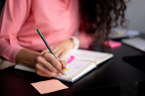 Close up of an unrecognizable businesswoman writing notes in her notebook using a pen