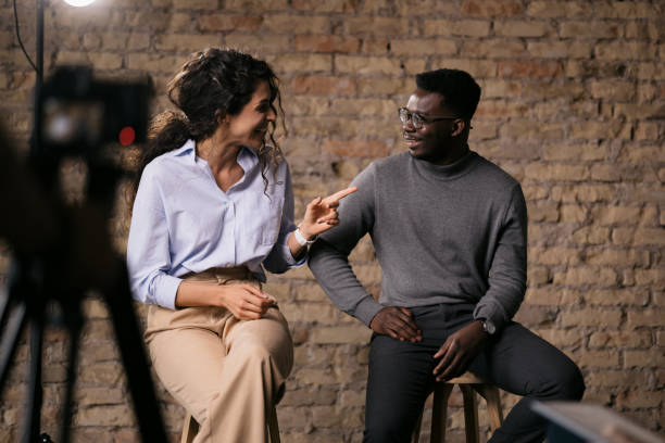 Diverse couple of models giving an interview in a studio Happy diverse couple of models giving an interview in a studio, smiling and gesturing with their hands while they talk, enjoying the backstage pre press stock pictures, royalty-free photos & images