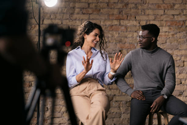 Diverse couple of models giving an interview in a studio Happy diverse couple of models giving an interview in a studio, smiling and gesturing with their hands while they talk, enjoying the backstage media interview photos stock pictures, royalty-free photos & images