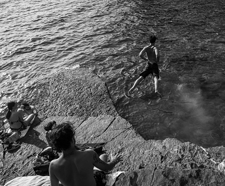 Porto Venere, Italy - June 18, 2022: young man dives into the sea among the rocks while other people are watching