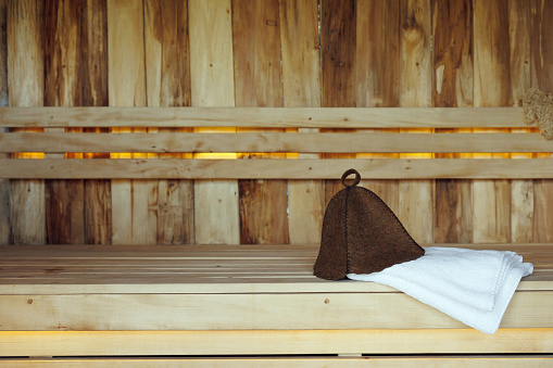 Bath hat and white towel lying on a bench from wooden planks in the sauna