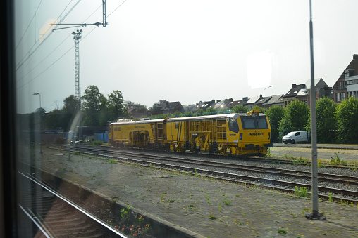 Lier, Vlaams-Brabant, Belgium - June 18, 2022: blurred view photographed from a passenger window in a moving train on Flemish landscape. View on yellow locomotive from the Belgian national company technical maintenance Infrabel