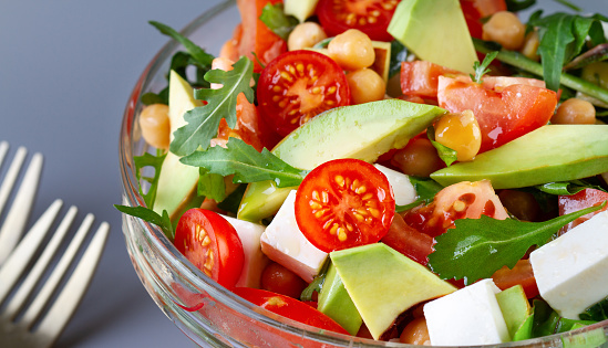 Vegetable salad of tomato and avocado with arugula in a cup close-up