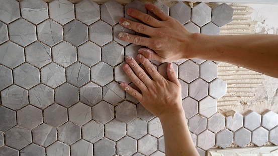 The worker presses the tile with his hands while gluing the tile. The working tiler mounts the tile on the wall, presses it with his hands. The master glues a mosaic of ceramic tiles.