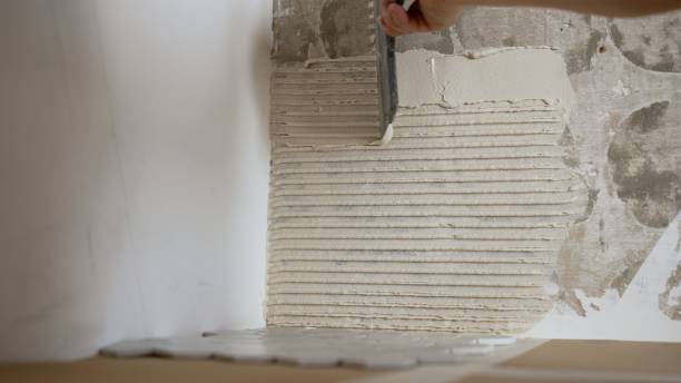 istock Application of tile adhesive with a ribbed trowel. With a special ribbed spatula, the builder applies the mortar to the wall, smoothes it, for laying tiles on the wall. Application of tile adhesive, ceramic mosaic tiles. 1404034790