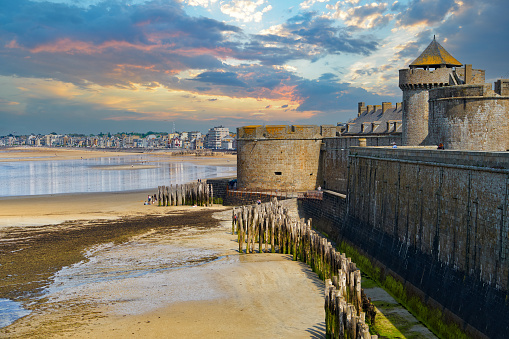 Skyline of the English Channel coast and the ancient fortress walls of the city of Saint-Malo during the ocean low tide in the evening against a dramatic sky. Brittany region, France