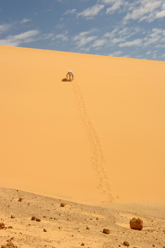 Man crawling up a sand dune in the western Sahara of Egypt.