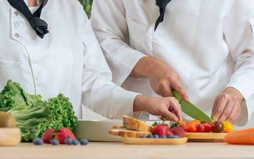 Selective focus on hands of professional chef wearing white uniform, using knife, cutting vegetable, cooking and preparing healthy food or meal for restaurant or hotel service