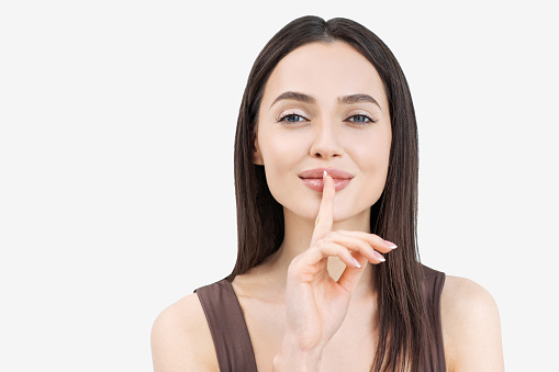 Close up of  young female saying 'shh', asking to keep silent about her secret. Isolated on grey background studio shot.