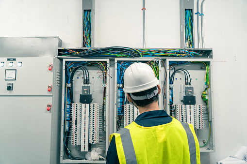 Behind Electrical Engineer or Electrician service working at Electrical panel room. Maintenance Engineer check or repair electrical control panel.
