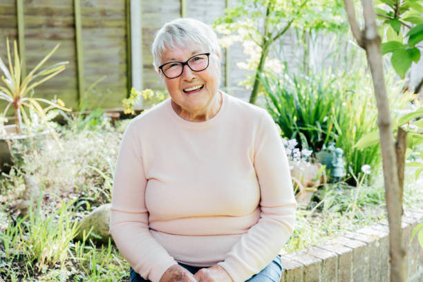 retrato de sorrindo avó aposentada e madura em óculos. mulher idosa feliz sorrindo sentada em seu jardim verde e desfrutando de estilo de vida de aposentadoria. foco seletivo. - senior adult senior women 80 plus years grandmother - fotografias e filmes do acervo