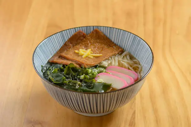 Japanese food deep-fried kitsune udon soba noodle in a bowl isolated on wooden table top view