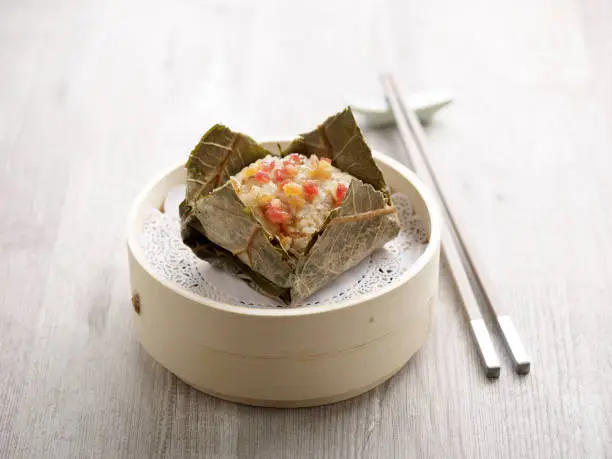 Steamed Glutinous Rice with Chicken Wrapped in Lotus Leaf served in a wooden bowl with chopsticks isolated on mat side view on grey marble background